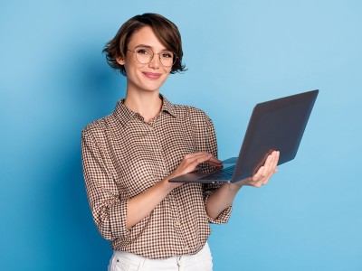 Jonge vrouw met een laptop in de hand, ze heeft een blije emotie omdat ze volledig mee is met de informatica dankzij Syntra AB